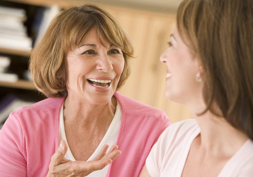 Two Women Sitting In Living Room Talking And Smiling