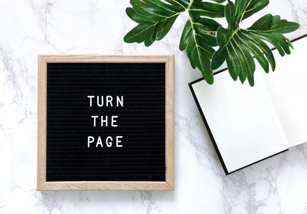 blank notebook, plant, and board with "turn the page"